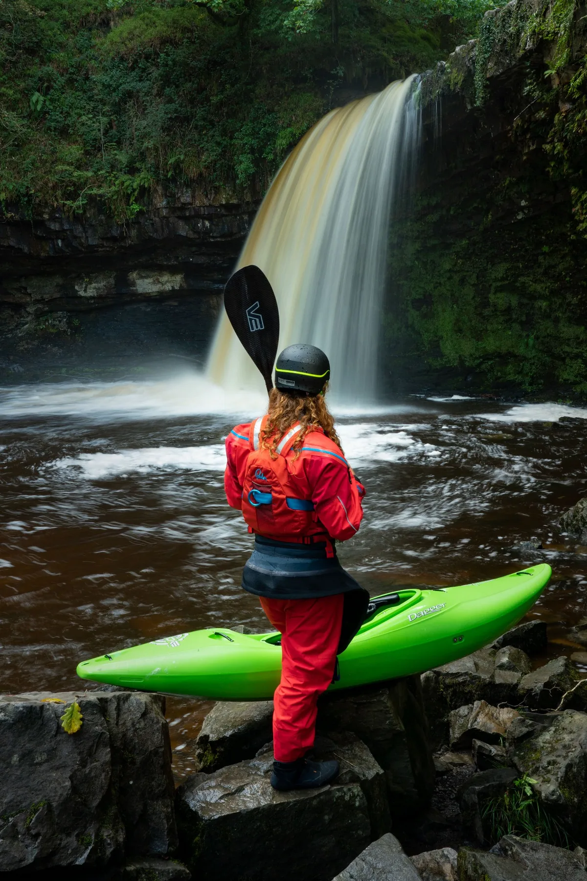Whitewater kayaker in a red paddling drysuit beside a waterfall
